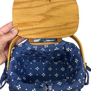 May include: A blue and white fabric-lined basket with a wooden lid and handles. The basket has a floral pattern and is perfect for storage or carrying small items.