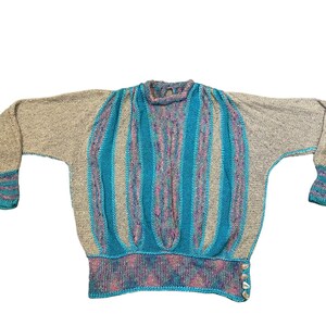 May include: A blue, gray, and pink striped sweater with a round neckline and long sleeves. The sweater has a button on the side.