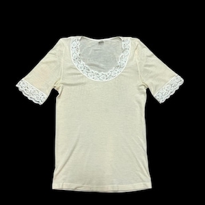 May include: A cream-coloured, short-sleeved t-shirt with a white lace trim around the neckline and sleeves.