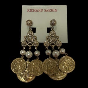 May include: Gold tone dangle earrings with a pearl and coin design. The earrings are on a white card with the text "Richard Serbin" printed in red.