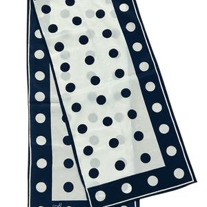 May include: A white silk scarf with a navy blue border and polka dots. The scarf is folded in half and the ends are overlapping.