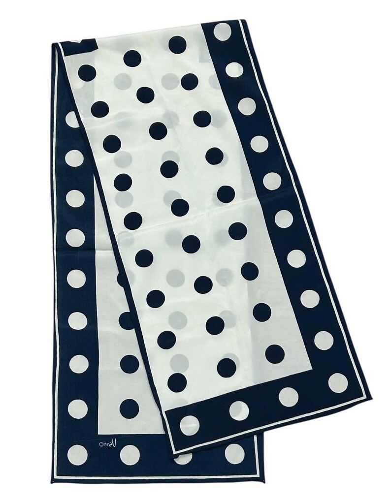 May include: A white silk scarf with a navy blue border and polka dots. The scarf is folded in half and the ends are overlapping.