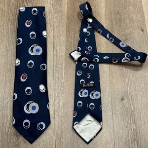 May include: A navy blue tie with a geometric pattern of white and blue circles with red accents. The tie has a label that reads "R. Brothers".