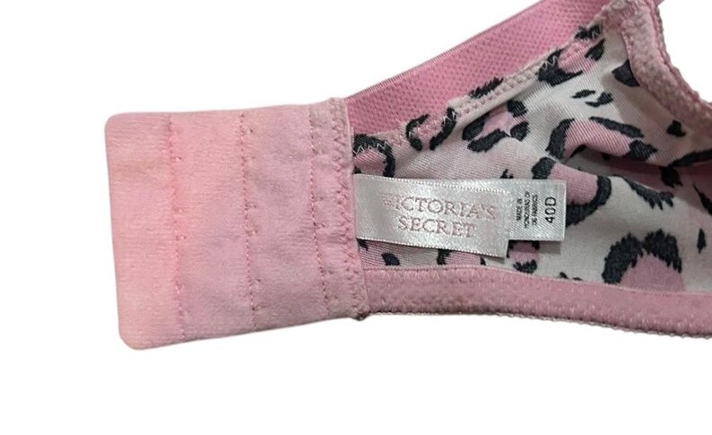 May include: Pink bra with a leopard print lining. The bra features a hook-and-eye closure and a tag that reads "VICTORIA'S SECRET" and size 40D. The bra is made of a soft, comfortable material.