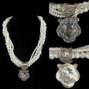 May include: A multi-strand pearl necklace with a decorative silver pendant. The necklace features various sizes of white pearls and a silver clasp. The pendant has an ornate, shield-like design. The necklace is displayed on a black mannequin.