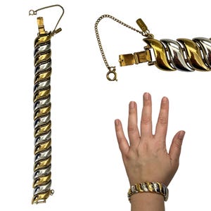 May include: A gold and silver-toned bracelet with a wave-like design. The bracelet has a safety chain and clasp. The bracelet is shown on a wrist and also displayed separately. The bracelet is approximately 7.5 inches long.