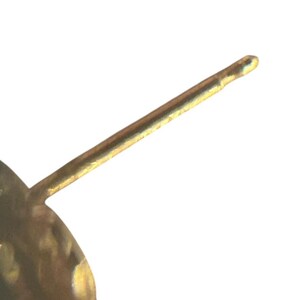 May include: Close-up of a gold-colored earring post. The post is a thin, straight rod with a rounded tip. The earring post is set against a white background.