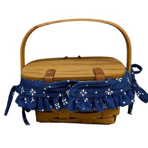 May include: A wooden picnic basket with a blue and white fabric lining and a brown leather handle.