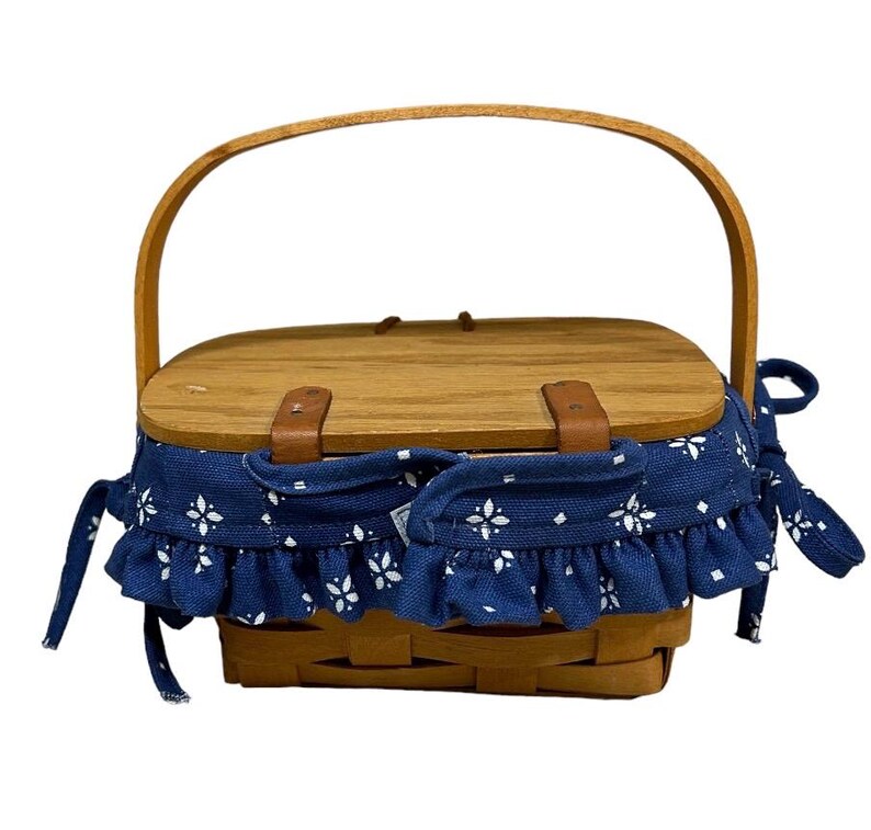 May include: A wooden picnic basket with a blue and white fabric lining and a brown leather handle.