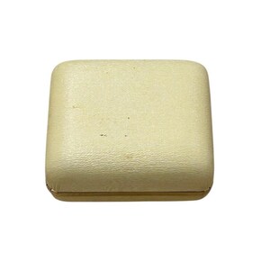 May include: A square, off-white jewelry box with a textured surface. The box has rounded corners and a gold-colored trim around the base. The box is closed and appears to be empty.