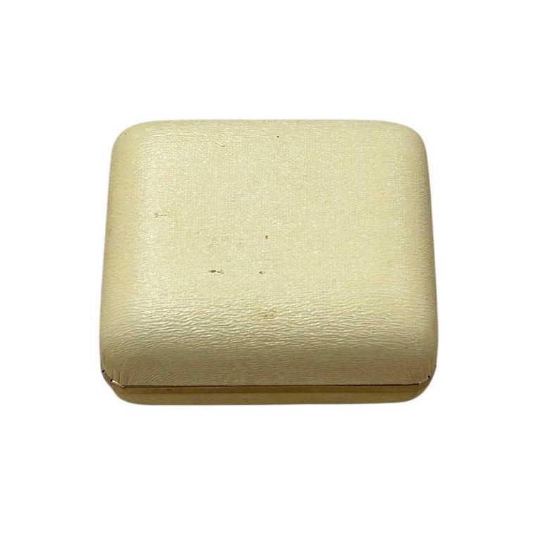 May include: A square, off-white jewelry box with a textured surface. The box has rounded corners and a gold-colored trim around the base. The box is closed and appears to be empty.