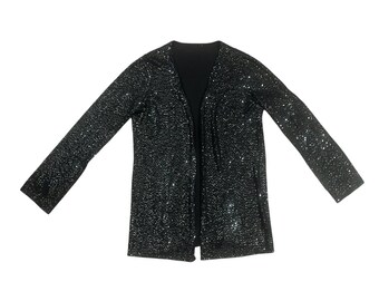 Puede incluir: Chaqueta negra de lentejuelas con mangas largas y frente abierto. La chaqueta tiene cuello en V y está cubierta de pequeñas lentejuelas reflectantes. La prenda está colocada sobre un fondo blanco.