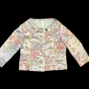 以下が含まれることがあります： ピンク、紫、緑の花柄の明るい色のジャケット。 ジャケットは丸い襟と3つのボタンが付いています。 袖は長く、生地はサテンの光沢があります。