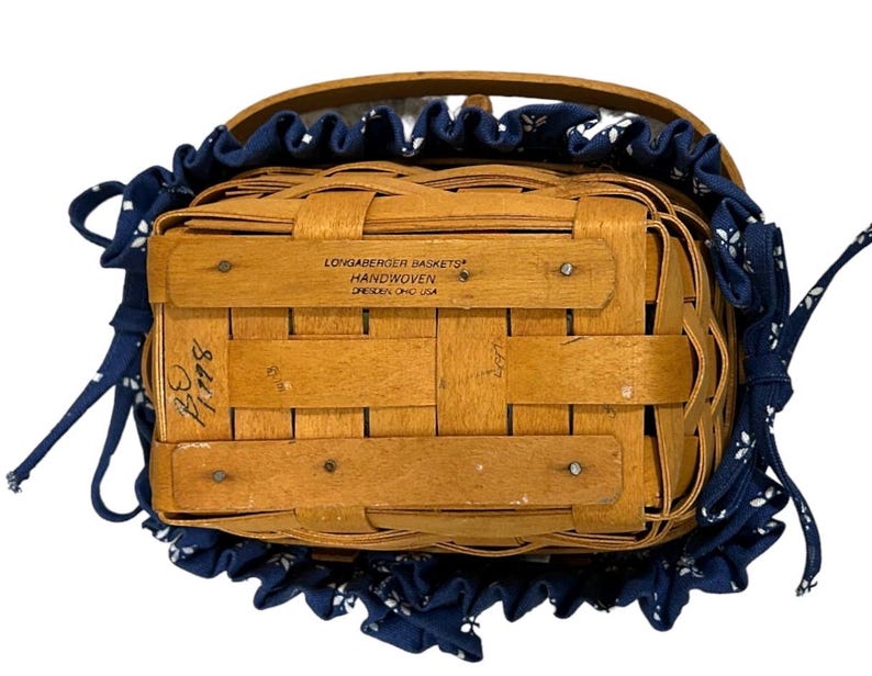 May include: A Longaberger Baskets handwoven basket with a blue and white fabric liner. The basket has a label that reads "Longaberger Baskets Handwoven  Dresden, Ohio USA".