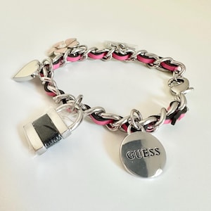 May include: A silver bracelet with a chain-link design, incorporating black and pink woven sections. It has charms including a heart, a padlock, a flower, and a round pendant with the word "GUESS".