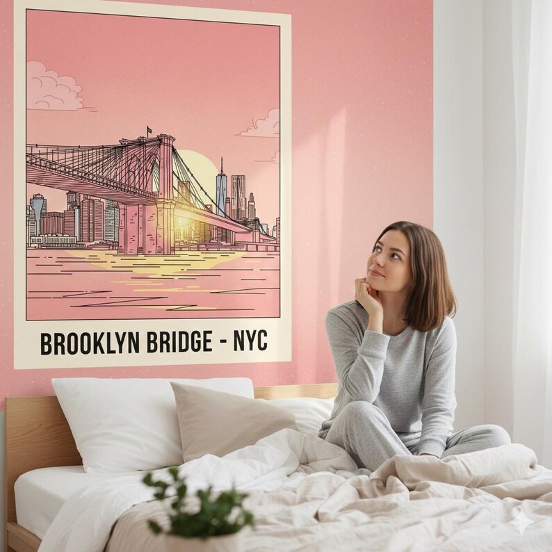 May include: A framed poster featuring a line drawing of the Brooklyn Bridge in New York City, with a pink and yellow sunset in the background. The text "BROOKLYN BRIDGE - NYC" is at the bottom. The poster is hanging on a pink wall.