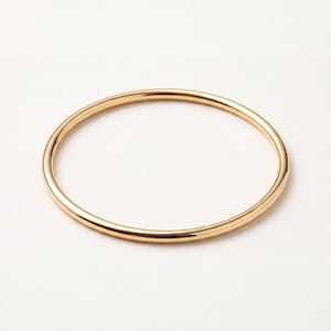 May include: A simple, circular gold bangle bracelet with a smooth, polished, and reflective surface. The jewelry piece features a continuous, thin, rounded band design that maintains a consistent thickness throughout its entire circumference.
