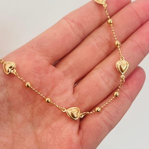 May include: A gold bracelet with heart-shaped charms and small round beads. The delicate bracelet is made of a thin chain. The heart charms are evenly spaced along the chain, creating a romantic and elegant design. The bracelet is likely to be around 18 cm in length.