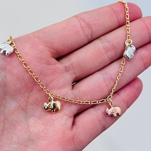 May include: Gold-toned chain bracelet with five elephant charms in gold and silver tones. The bracelet is displayed on a light background, showcasing the jewelry's design and details. The elephant charms are small and detailed.