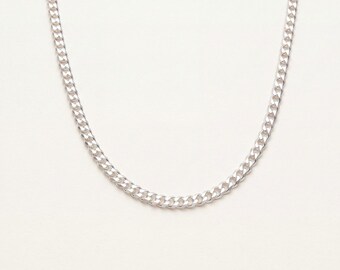 May include: A silver-toned curb chain necklace featuring a series of interlocking, flattened oval links. The metal has a polished, reflective finish that catches the light, creating a consistent, uniform pattern throughout the entire length of the chain.