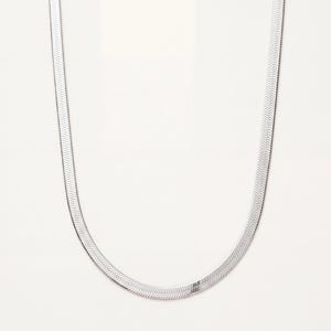 Puede incluir: Un collar de cadena tipo espiga en tono plateado con un diseño plano y flexible que presenta un patrón en forma de V repetitivo. Los eslabones metálicos están estrechamente entrelazados para crear una superficie lisa y continua que refleja la luz.