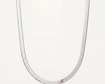 May include: A silver-toned herringbone chain necklace featuring a flat, flexible design with a repeating V-shaped pattern. The metallic links are tightly woven together to create a smooth, continuous surface that reflects light along the entire length.