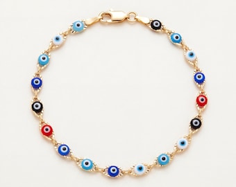Puede incluir: Una pulsera de cadena dorada con una serie de pequeños dijes circulares en forma de ojo en varios colores, incluyendo azul claro, azul oscuro, rojo y negro. La pulsera está asegurada con un cierre de mosquetón de color dorado.