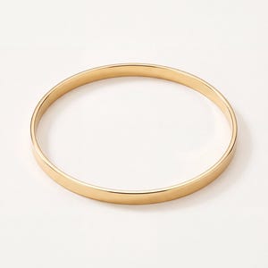May include: A thin, circular bangle bracelet with a polished, smooth gold-tone finish. The jewelry piece features a simple, continuous band design with a reflective surface that catches the light, creating a clean and uniform appearance throughout.