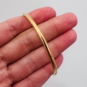 Op de afbeelding: Een goudkleurige armband. De armband is een eenvoudige, gladde band met een afgerond profiel. De goudkleur is helder en reflecterend, wat wijst op een gepolijste afwerking. Een klassiek sieraad.