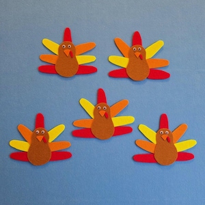 May include: Five felt turkey decorations. Each turkey has a brown body, red wattle, and a fan of colorful feathers in red, orange, and yellow. The turkeys are arranged on a blue background.