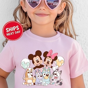 A young girl wearing a pink t-shirt with a cartoon character design and heart-shaped sunglasses.