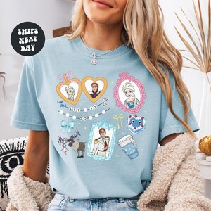 A woman wearing a light blue t-shirt with various cartoon characters and designs printed on it.