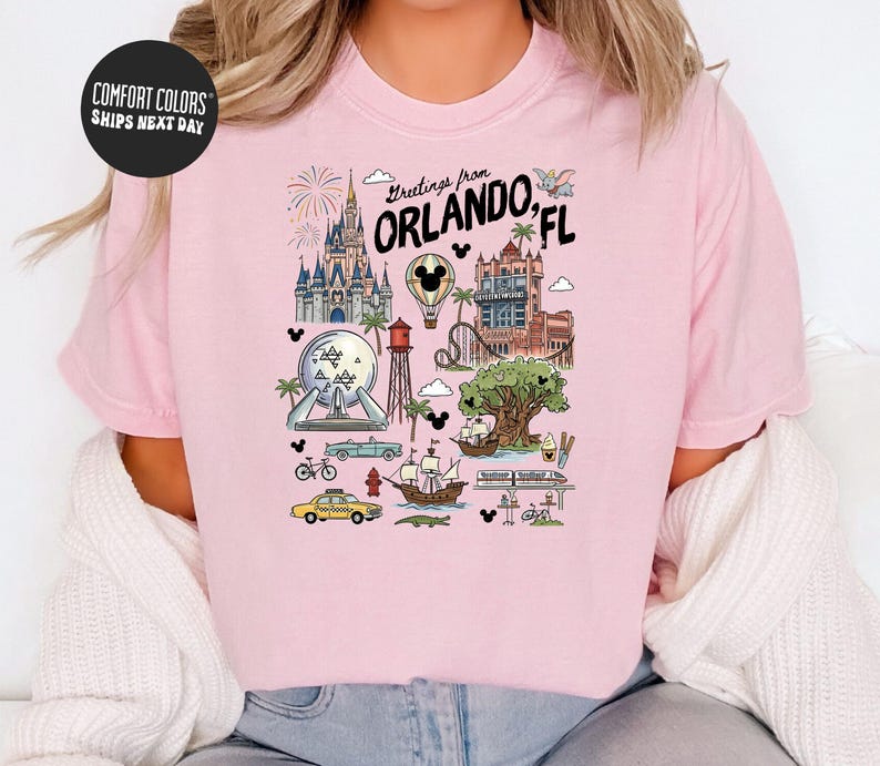 A pink t-shirt with a graphic design depicting various landmarks and attractions in Orlando, Florida, including Disney World, the Walt Disney World Resort, and other iconic sites.