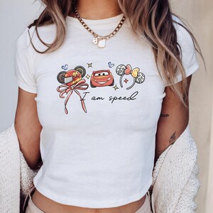 A woman wearing a white t-shirt with a graphic design featuring cartoon characters and the text "I am speed".