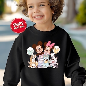 A young girl wearing a black sweatshirt with a cartoon character design on it, smiling and looking at the camera.