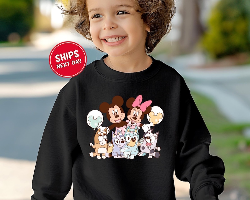 A young girl wearing a black sweatshirt with a cartoon character design on it, smiling and looking at the camera.