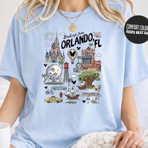 A woman wearing a light blue t-shirt with a graphic design depicting various landmarks and icons associated with Orlando, Florida.
