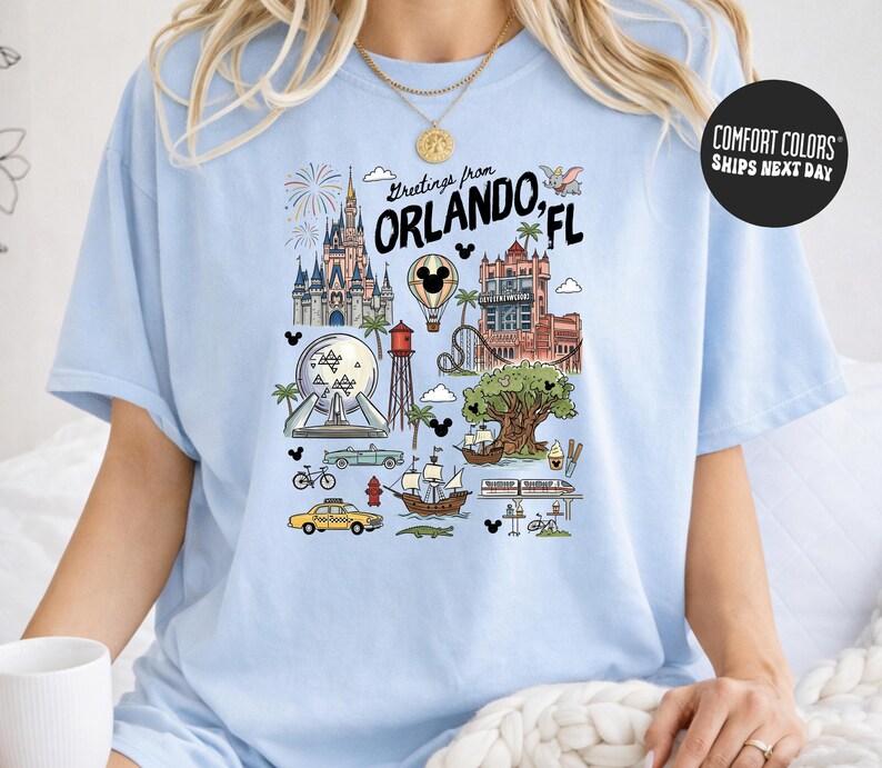A woman wearing a light blue t-shirt with a graphic design depicting various landmarks and icons associated with Orlando, Florida.