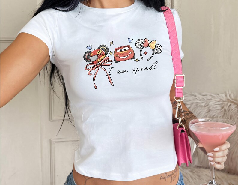 A person wearing a white t-shirt with a graphic design and holding a pink drink.
