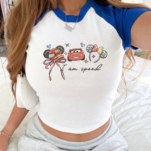 A person wearing a white and blue shirt with a graphic design featuring cartoon characters and the text "I am speed".