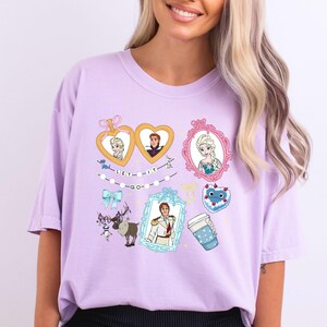 A woman wearing a pink t-shirt with various cartoon characters and illustrations, including Elsa from Frozen, a heart, a cup, and other whimsical elements.
