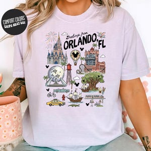 A person wearing a white t-shirt with a graphic design depicting various landmarks and attractions from Orlando, Florida, including Disney World, the Walt Disney World Resort, and other iconic sites.