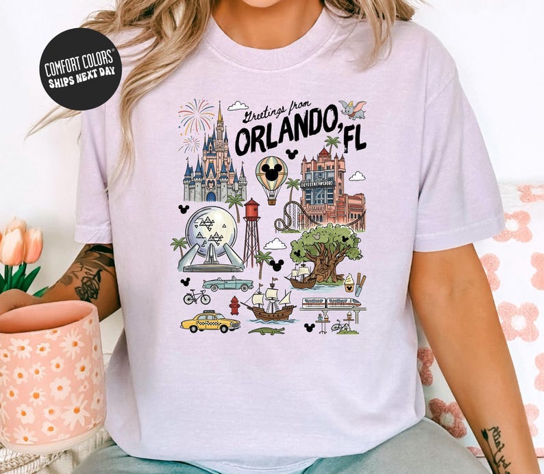 A person wearing a white t-shirt with a graphic design depicting various landmarks and attractions from Orlando, Florida, including Disney World, the Walt Disney World Resort, and other iconic sites.