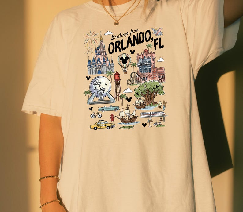 A person wearing a white t-shirt with a graphic design depicting various landmarks and attractions from Orlando, Florida.