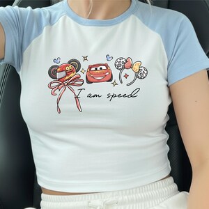 A person wearing a white t-shirt with a graphic design featuring cartoon characters and the text "I am speed".