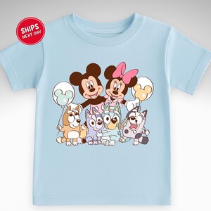 A light blue t-shirt with a cartoon image of various Disney characters, including Mickey Mouse, Minnie Mouse, Bluey the Cat, and other iconic figures.