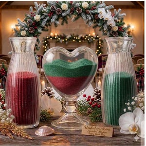 Puede incluir: Dos jarrones de vidrio estriado altos llenos de arena roja y verde, flanqueando un recipiente central de vidrio en forma de corazón con arena verde y roja en capas. Una pequeña placa de madera al frente dice: Unidad en Arena, Navidad Mágica, Rojo y Verde Pino.
