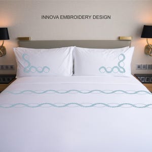 May include: White bed linen set with light blue embroidered wave design. The set includes two pillowcases and a fitted sheet. The text "INNOVA EMBROIDERY DESIGN" is at the top. The bed is in a hotel room setting.