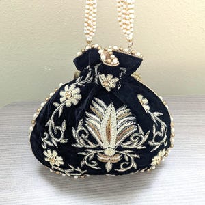 May include: Black velvet drawstring bag with intricate gold and cream floral embroidery. The bag features a beaded handle and is adorned with pearls. A decorative accessory for special occasions.