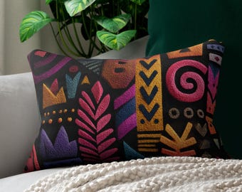 May include: A rectangular decorative pillow with a black background and colorful embroidered tribal patterns. The patterns include pink, purple, yellow, and blue shapes. The pillow is on a gray sofa with a white blanket.